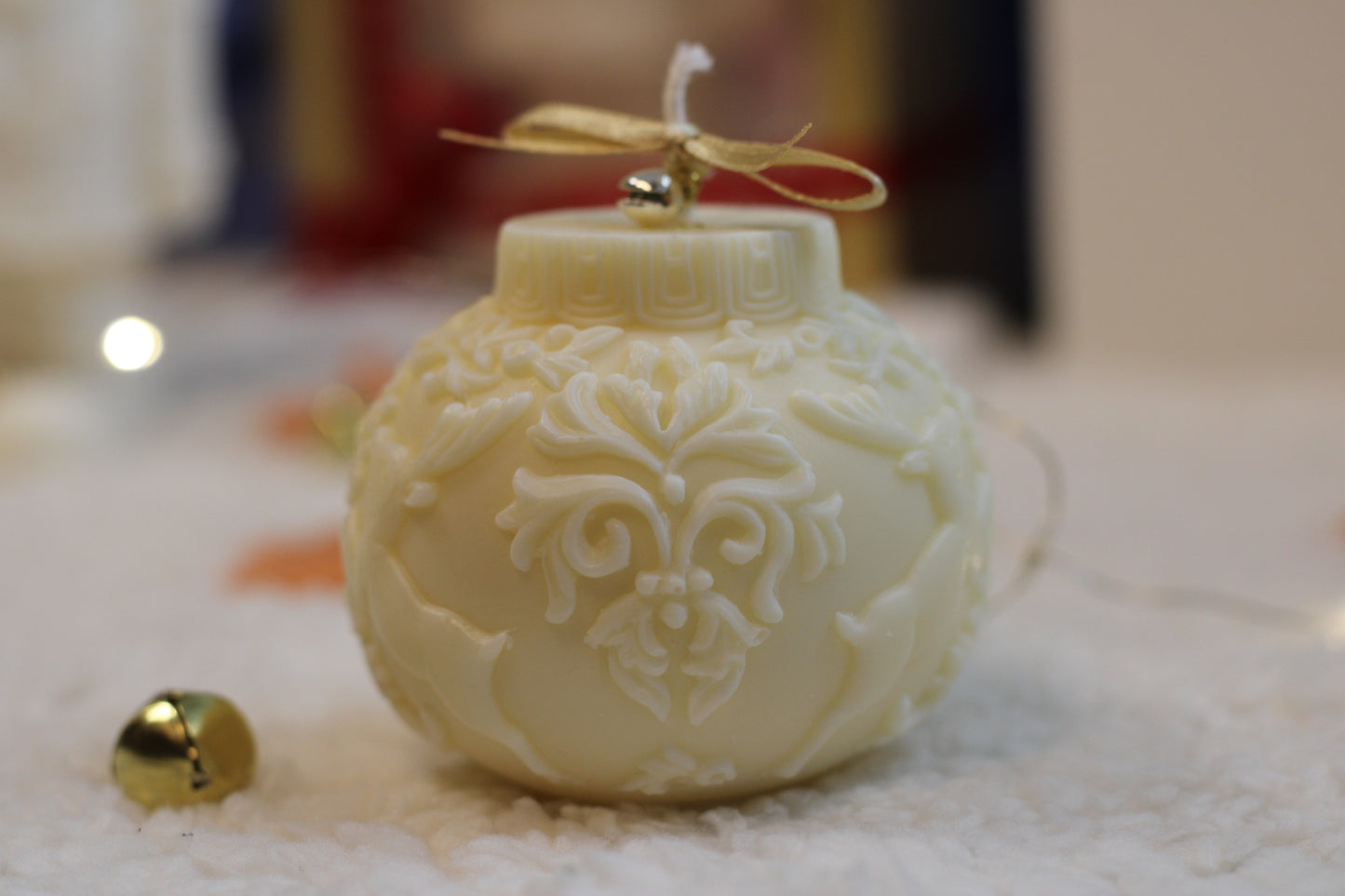 Handgefertigte runde cremefarbene Weihnachtskerze mit Rentier-Relief, goldener Schleife und Glöckchen auf festlich dekoriertem Hintergrund.